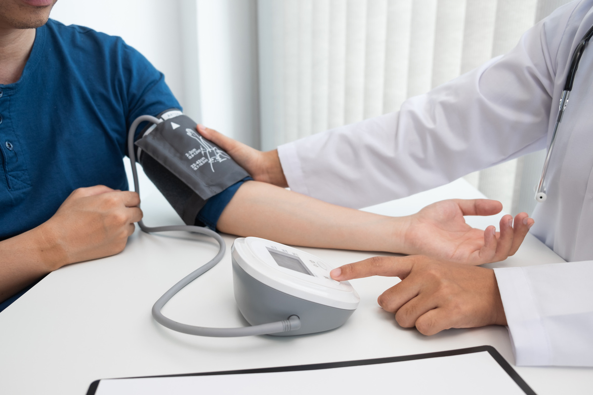 The doctor is measuring blood pressure on the patient arm with the blood pressure monitor in the hospital.